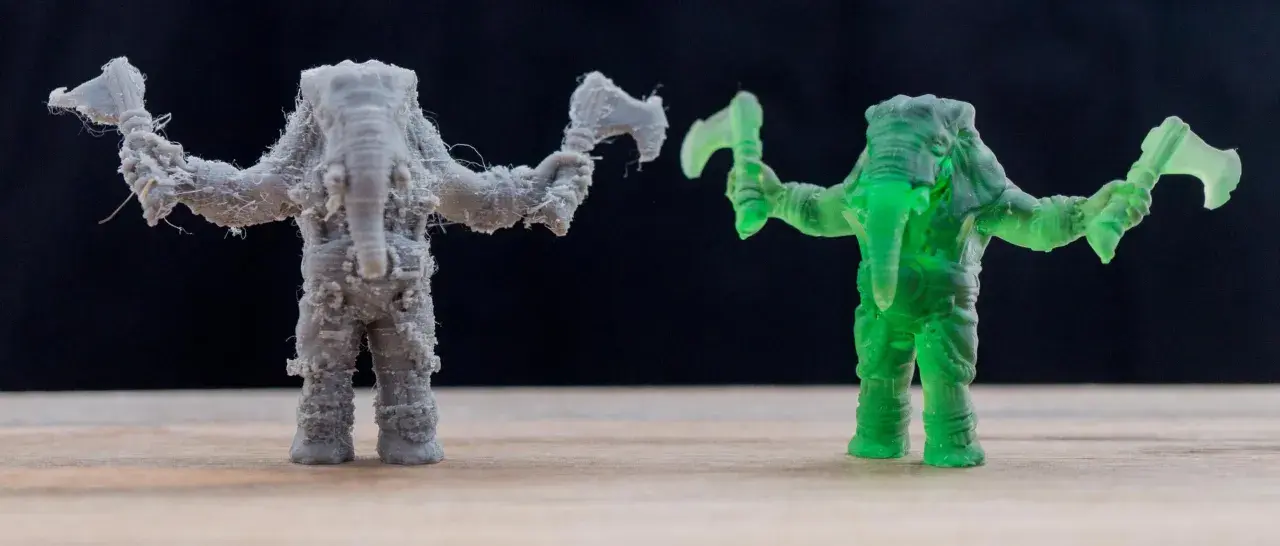 A grey FDM printed elephant warrior with stringing, and a translucent green resin printed elephant warrior, showcasing the difference between FDM vs resin printing.