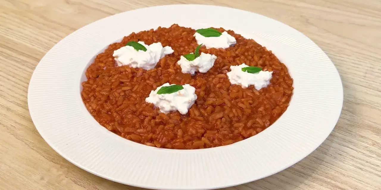 Un invitante risotto al pomodoro, arricchito da ciuffi di ricotta fresca e basilico, pronto per essere gustato.