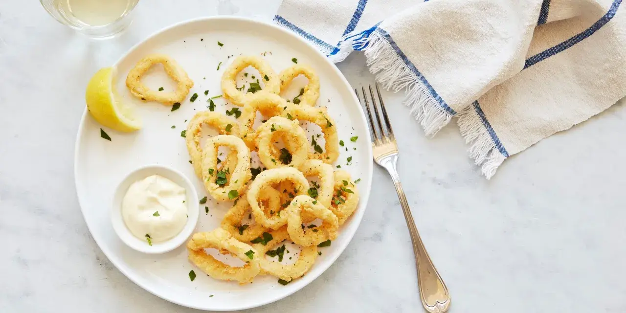 Crujientes calamares a la romana, servidos con limón y salsa tártara en un plato blanco.