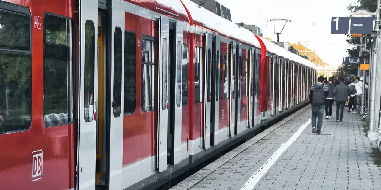 Czerwony pociąg na stacji. Ludzie czekają na peronie, zastanawiając się, jak zwrocic bilet.