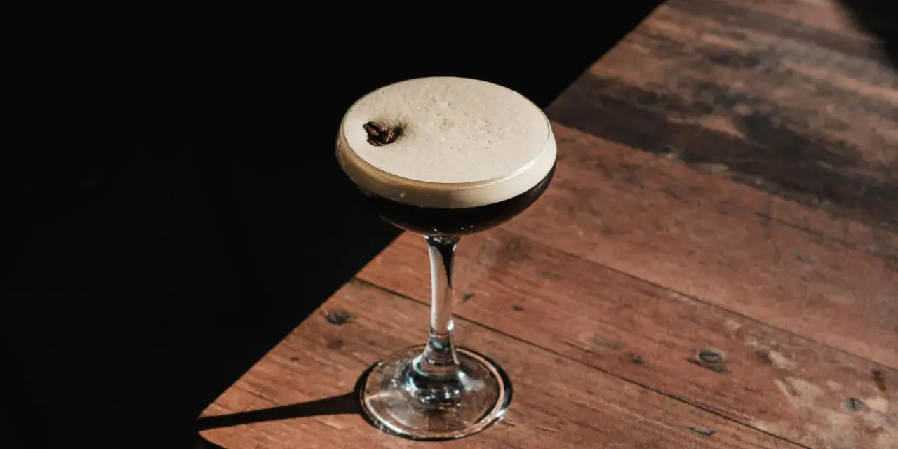 Espresso Martini przepis: elegancki koktajl z pianką i ziarnem kawy na drewnianym blacie.