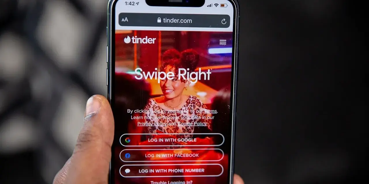 Telefon z aplikacją Tinder. Widoczne opcje logowania: Google, Facebook, numer telefonu. Czas na skróty na Tinderze!
