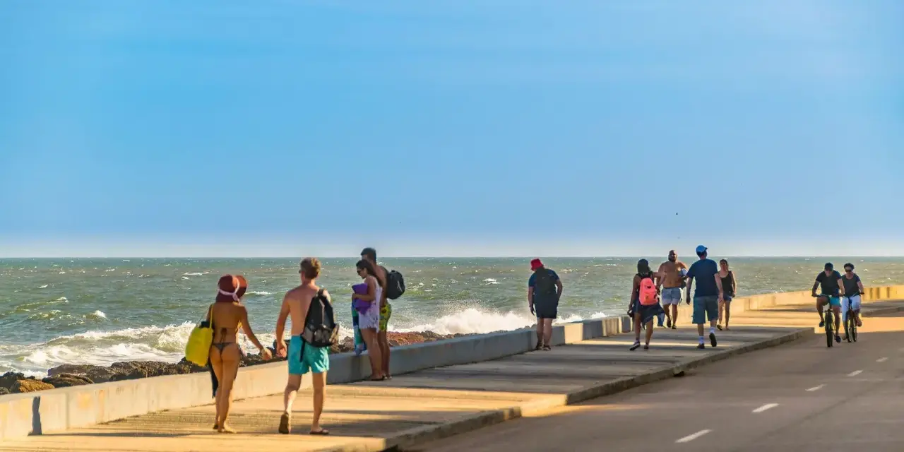 Ludzie spacerują i jeżdżą na rowerach wzdłuż promenady nad oceanem w słoneczny dzień.