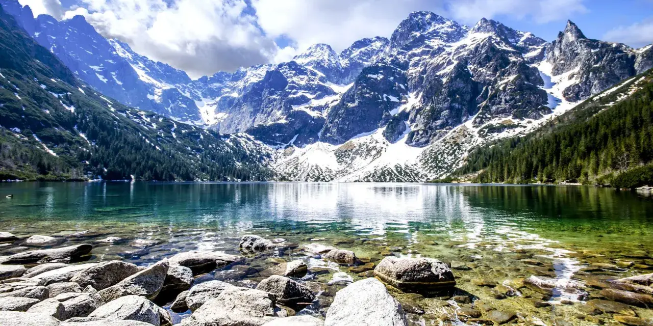 Morskie Oko, jedne z najpiękniejszych gór w Polsce, otoczone ośnieżonymi szczytami i zielonymi lasami, odbija się w krystalicznie czystej wodzie.