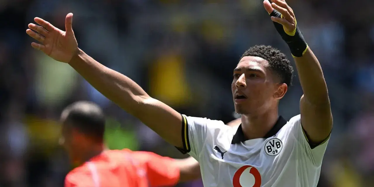 Jude Bellingham, con los brazos en alto, celebra un gol. El joven jugador del Dortmund, con su camiseta blanca, inspira a la afición.