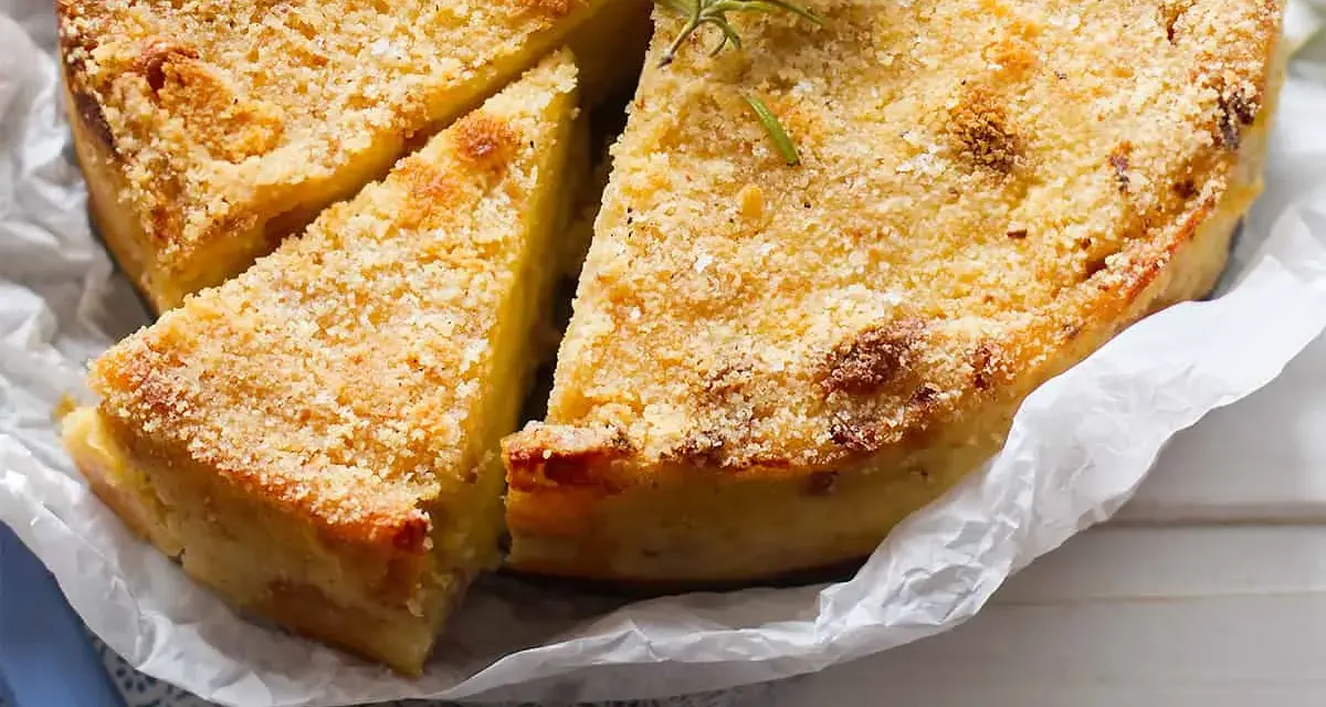 Delizioso gateau di patate dorato e croccante, guarnito con rosmarino fresco. Una fetta è già stata tagliata, invitando ad assaggiarlo.