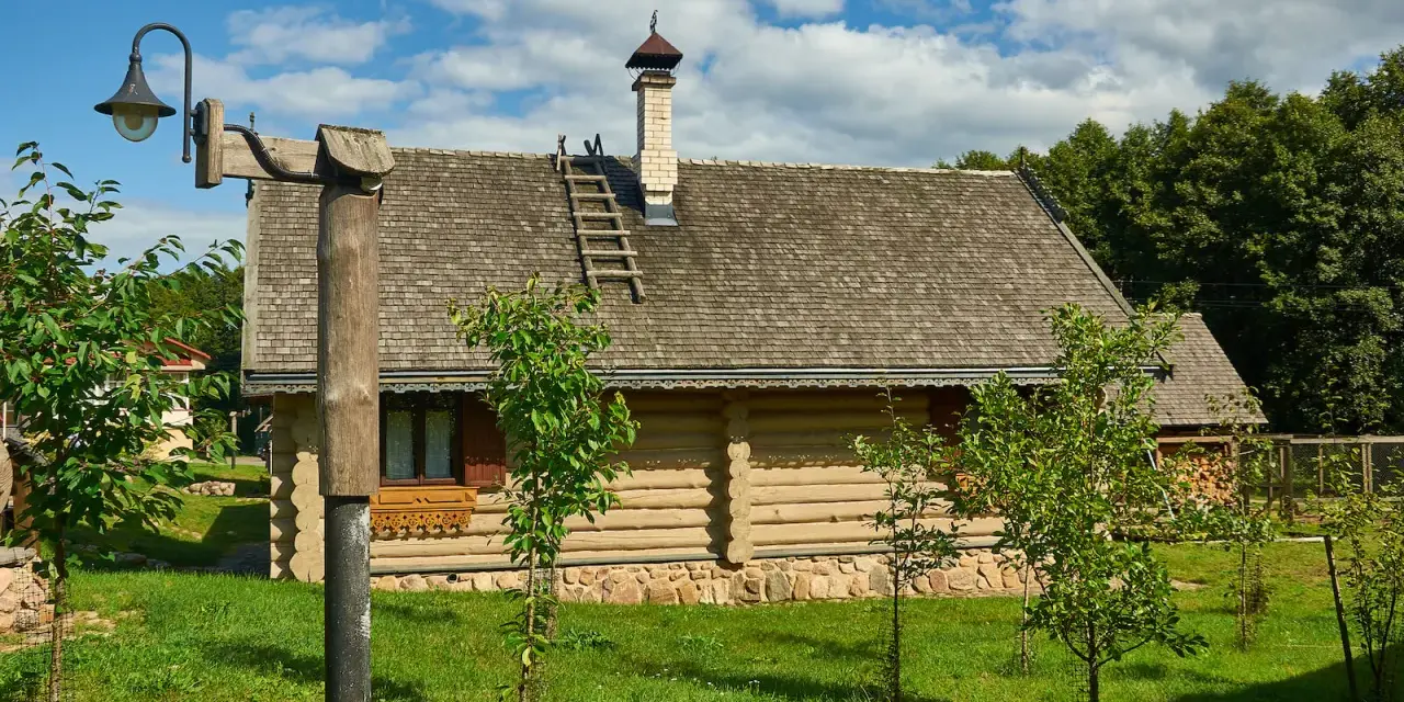 Drewniany dom z kamienną podmurówką i gontowym dachem, otoczony zielenią. To malownicze grunty rolne zabudowane, gdzie tradycja spotyka się z naturą.