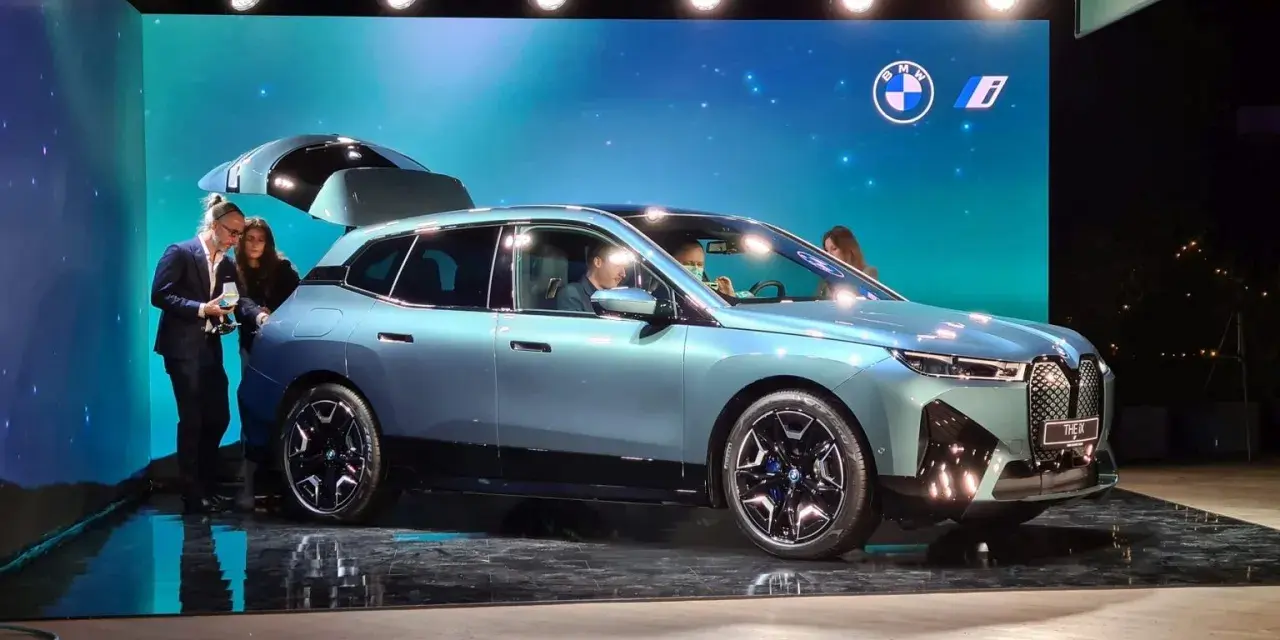 Jasnoniebieski elektryczny SUV BMW iX z otwartą klapą bagażnika na scenie.