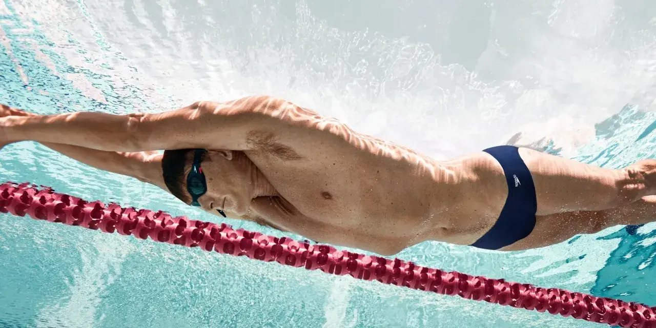 Un nageur en plein effort, profitant des bienfaits natation. La lumière joue sur son corps musclé, soulignant la puissance de ses mouvements sous l'eau.