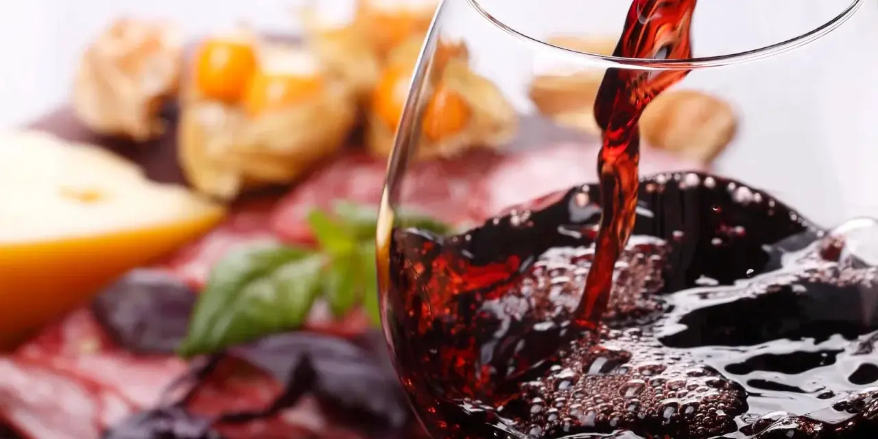 Rotwein wird in ein Glas gegossen, daneben Käse und Wurst. Welcher Wein hat am wenigsten Kalorien?