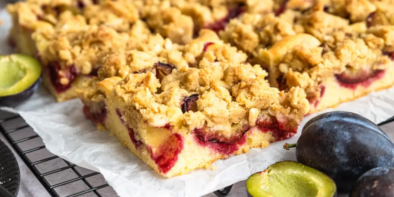 Saftiger Zwetschgenkuchen mit Streuseln, frisch gebacken und bereit zum Genießen. Daneben liegen frische Zwetschgen.