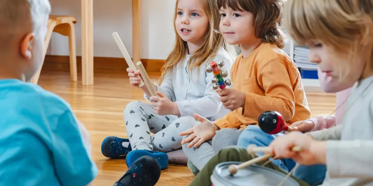 Kinder musizieren mit Holzstäben, Rasseln, einer Trommel und einem Maracas. Welche Instrumente gibt es?