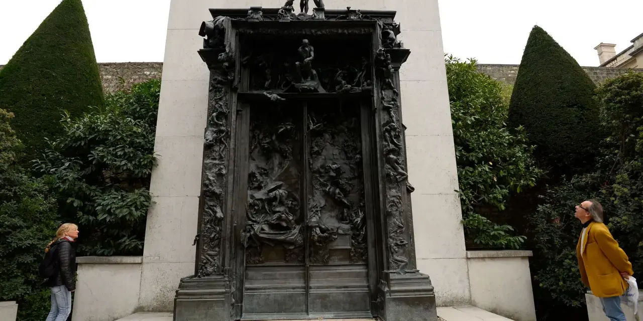 La Porte de l'Enfer de Rodin, une œuvre monumentale en bronze, se dresse au milieu d'un jardin. Deux visiteurs contemplent cette sculpture complexe.
