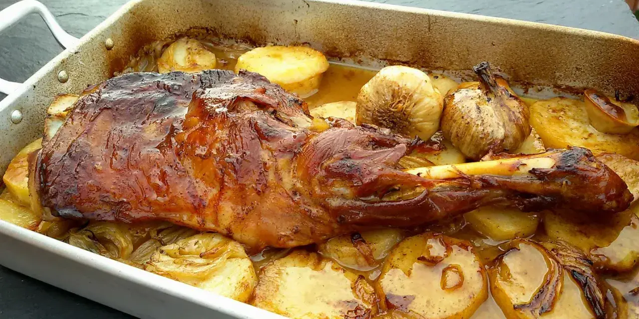 Delicioso cordero asado en una bandeja con patatas doradas y ajos enteros. Un festín para los sentidos.
