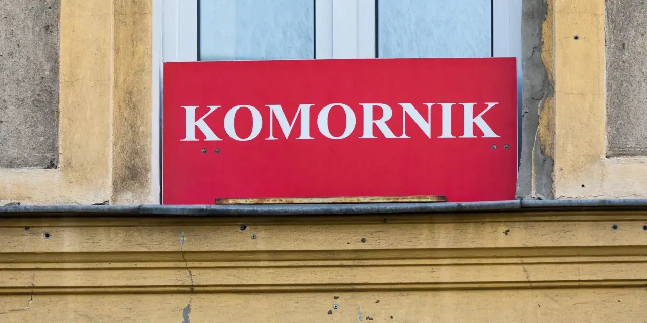 Czerwona tablica z napisem "KOMORNIK" na tle okna. Może to oznaczać zajęcie komornicze wynagrodzenia.