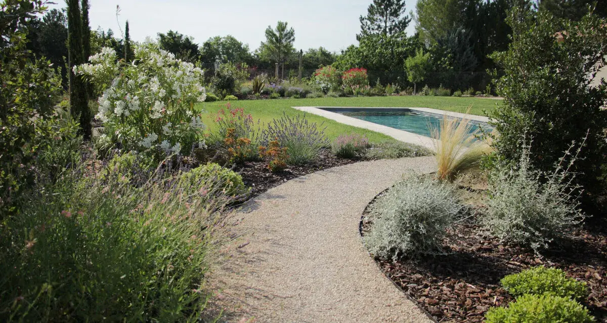 Une allée de jardin originale serpente vers une piscine, bordée de lavande, de fleurs blanches et d'arbustes verts.