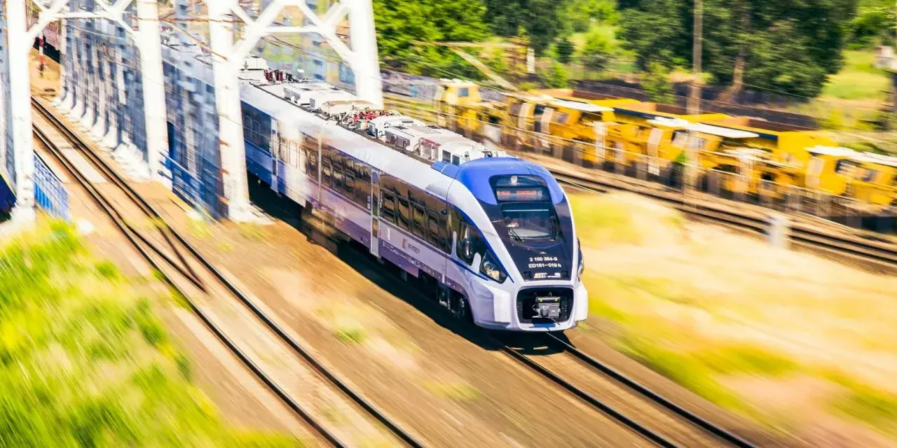 Nowoczesny pociąg PKP Intercity z niebieskim przodem mija biały most kolejowy.