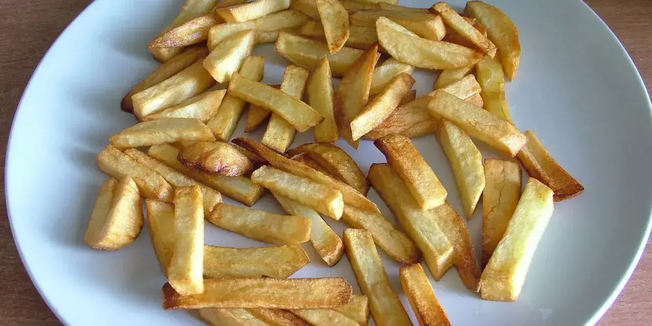 Złociste frytki z piekarnika na talerzu. Zastanawiasz się, ile kcal mają frytki z piekarnika? Oto porcja pysznych, pieczonych ziemniaków.