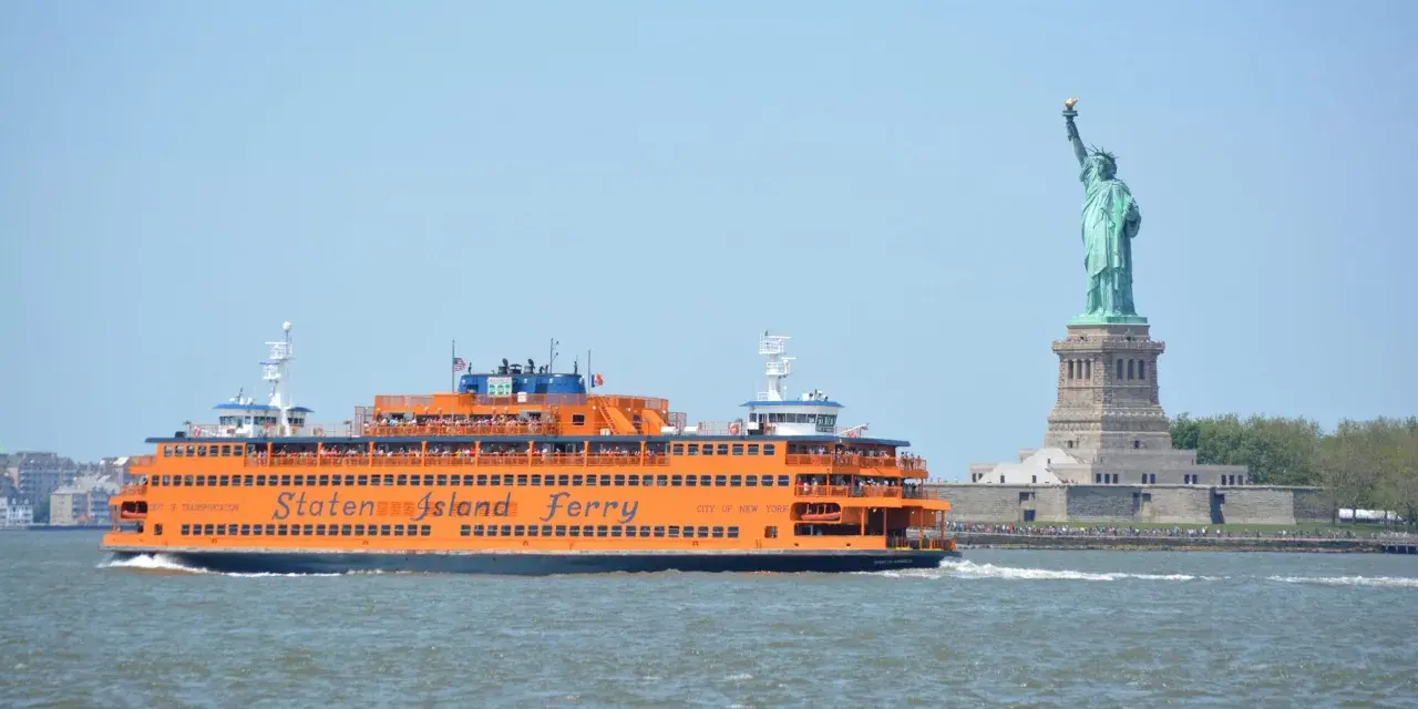Pomarańczowy prom Staten Island Ferry płynie obok Statuy Wolności.
