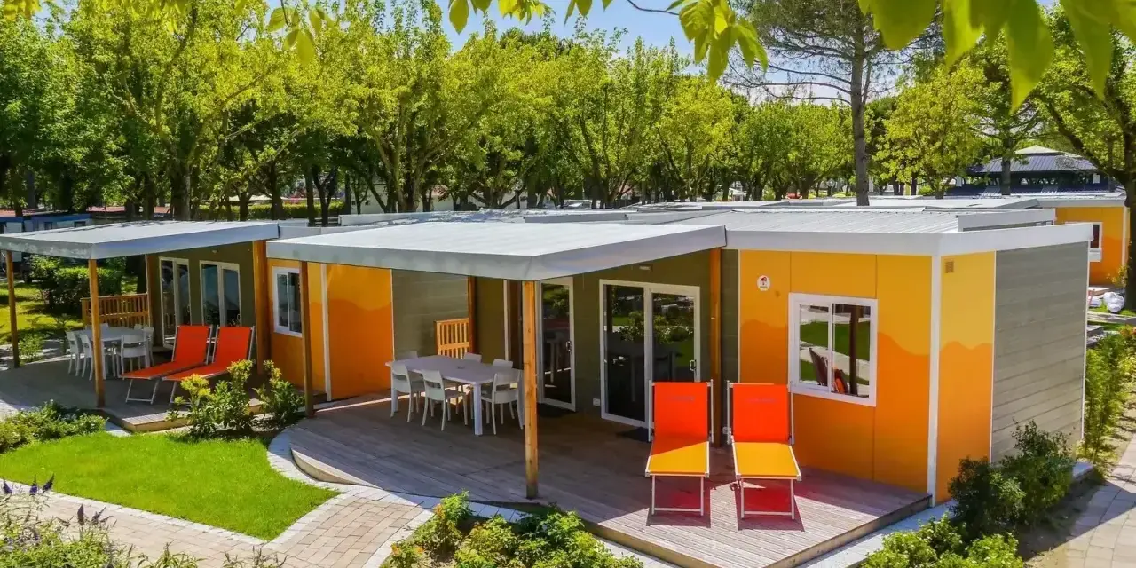 Kolorowe domki na kempingu, z tarasami i leżakami, otoczone zielenią. Prawdziwy camping garden paradiso!