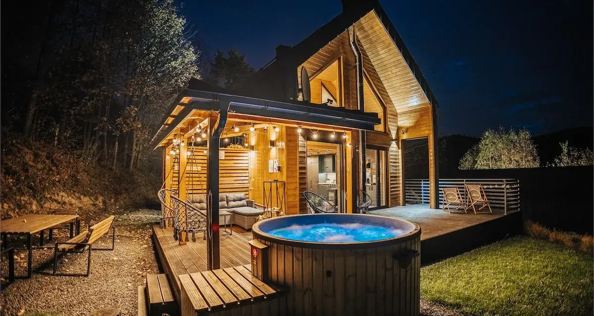 Drewniany domek z jacuzzi i tarasem, idealne miejsce na babia góra noclegi. Oświetlony girlandami, zaprasza do relaksu.