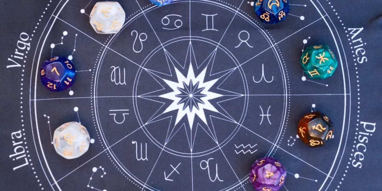 Kolorowe kostki z symbolami zodiaku i liczbami, leżące na tle z kołem horoskopowym. Każda liczba w numerologii ma swoje znaczenie.