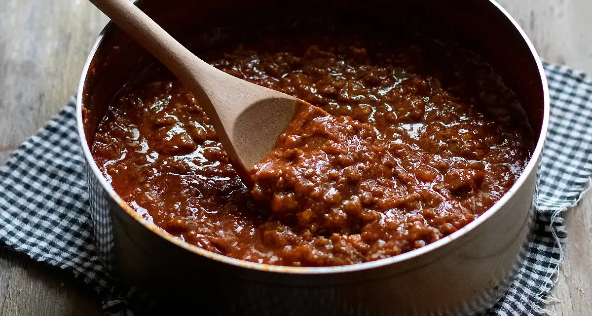 Un pentolino pieno di profumato ragù di carne, pronto per condire la pasta. Un cucchiaio di legno mescola la salsa densa e invitante.