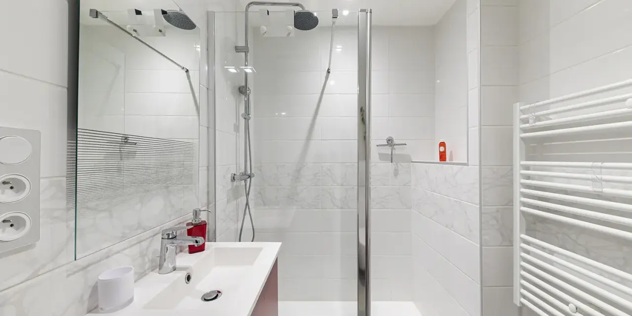 Salle de bain moderne, prête pour la prochaine étape de rénovation. Douche, lavabo et sèche-serviettes blancs.