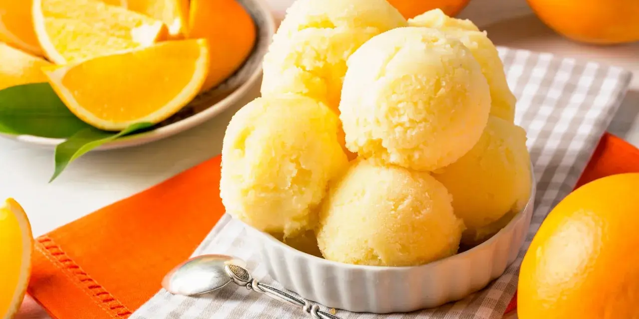 Erfrischendes orangen sorbet in einer Schale, umgeben von frischen Orangen und saftigen Orangenstücken. Ein Löffel liegt bereit.