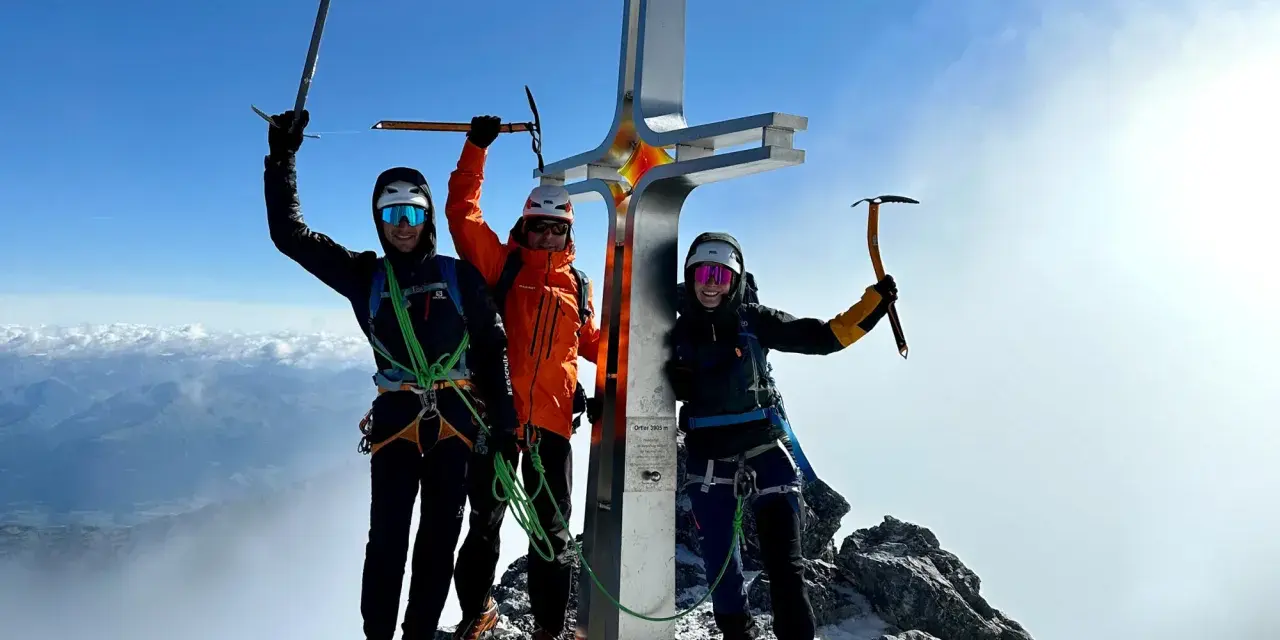 Drei Bergsteiger feiern am Gipfelkreuz des Ortler Normalwegs ihren Erfolg.