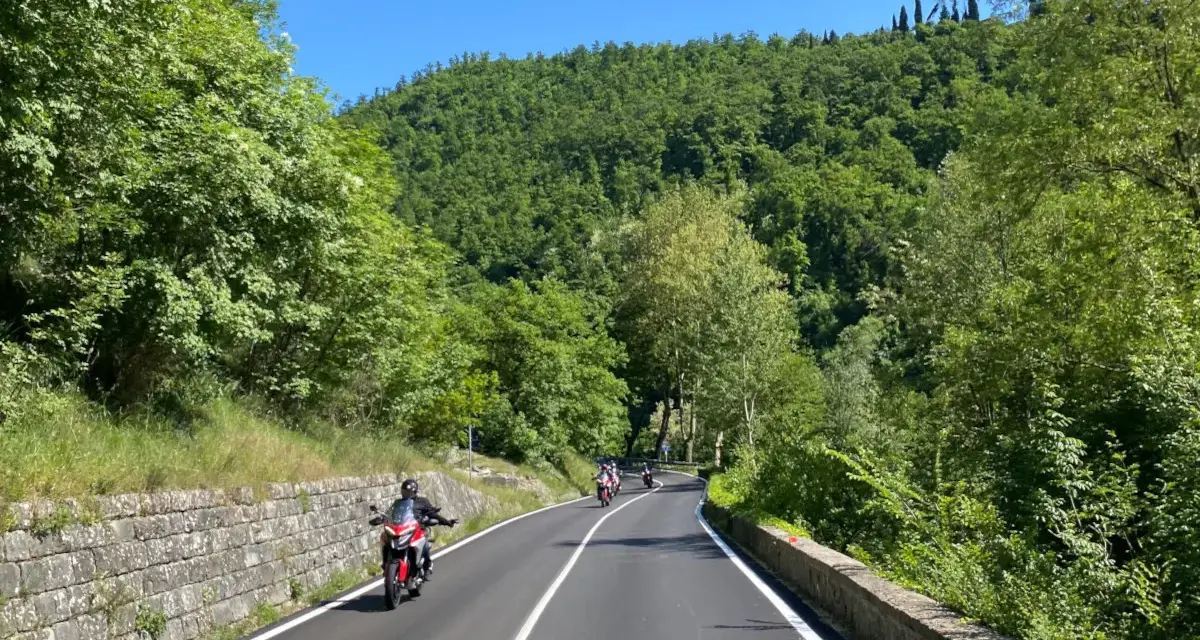 Motociclisti su strade panoramiche in Emilia Romagna, tra colline verdi e cielo azzurro.