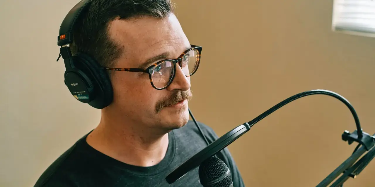 Mężczyzna w okularach i słuchawkach Sony nagrywa podcast. Dba o odpowiedni gain staging, by dźwięk był czysty.