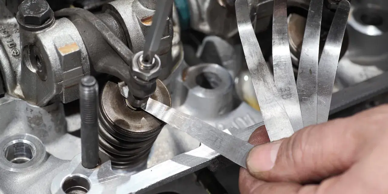 Mechanik sprawdza luzy zaworowe za pomocą szczelinomierza w silniku samochodowym.