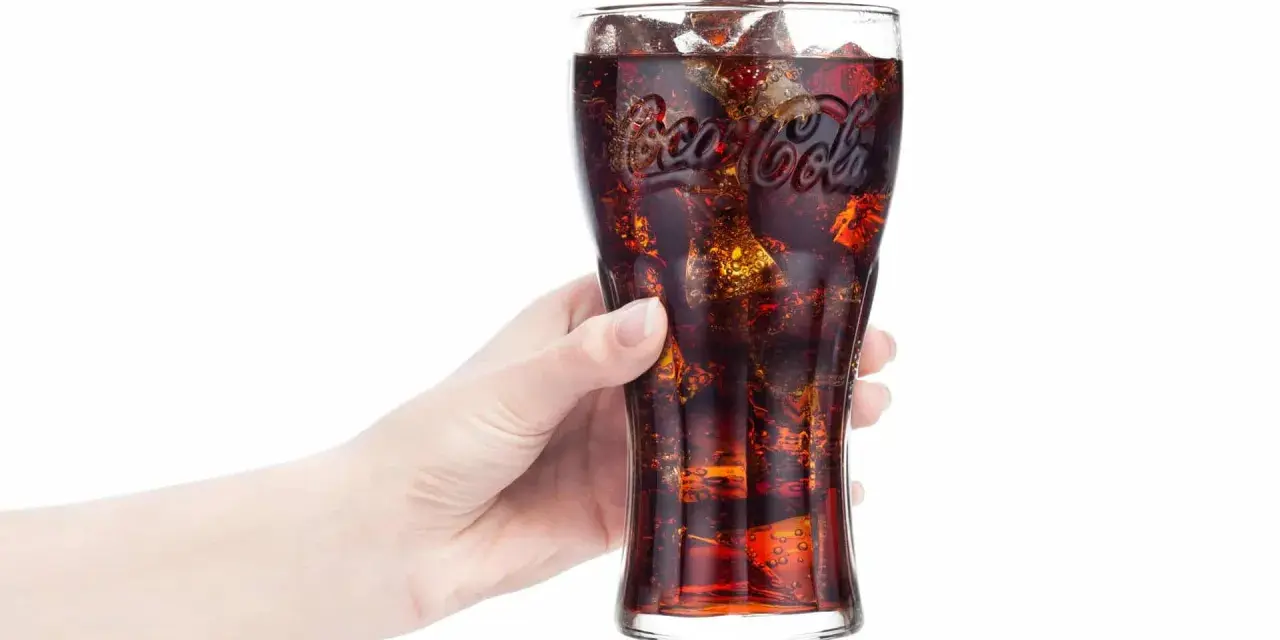 Hand hält Glas mit eiskalter Cola. Frage: Ist Cola in der Schwangerschaft erlaubt?