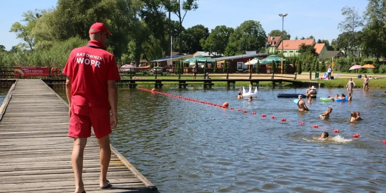 Ratownik WOPR czuwa nad bezpieczeństwem kąpiących się na Jeziorze Skępe. Ludzie pływają i relaksują się w wodzie.