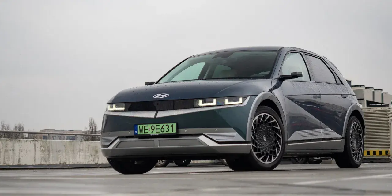 Hyundai Ioniq 5, z charakterystycznymi światłami i felgami, prezentuje swoje imponujące wymiary na mokrym parkingu.