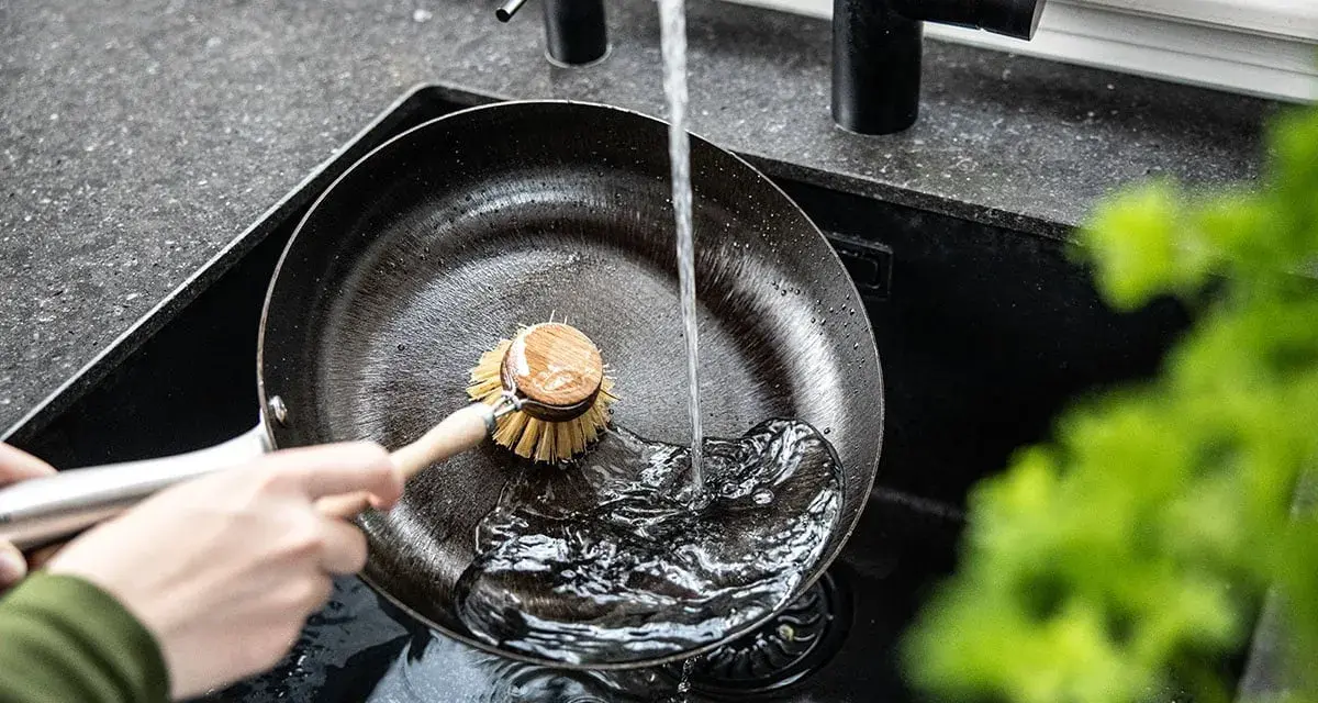 Mycie patelni żeliwnej pod bieżącą wodą za pomocą szczotki.