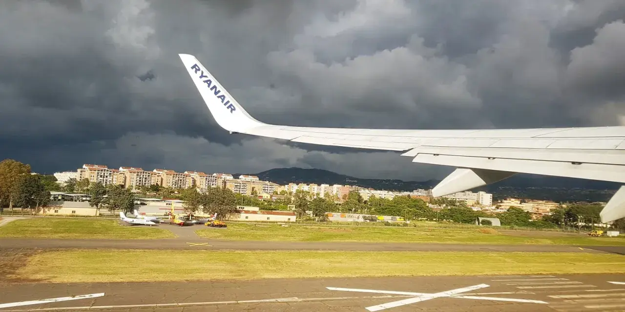 Skrzydło samolotu Ryanair nad lotniskiem, ciemne chmury na niebie.