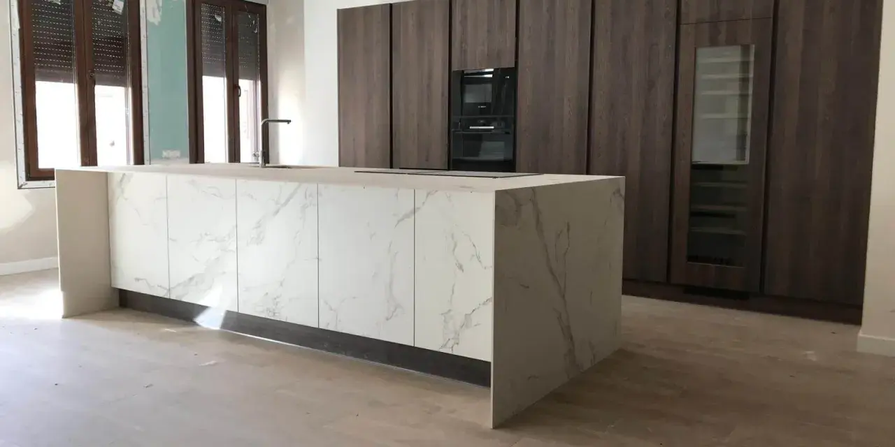 Isla de cocina moderna con encimera de mármol y armarios oscuros. Se aprecian las medidas de los muebles de cocina en el diseño.