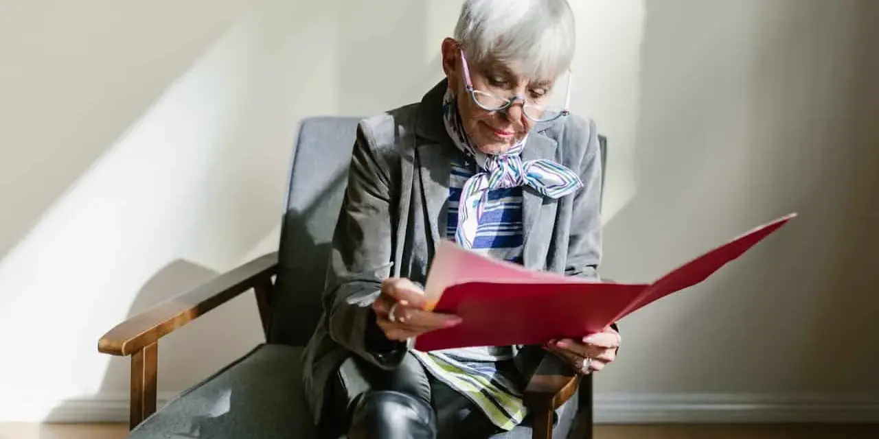 Une femme âgée, en pleine retraite, examine des documents artistiques dans un dossier rouge.