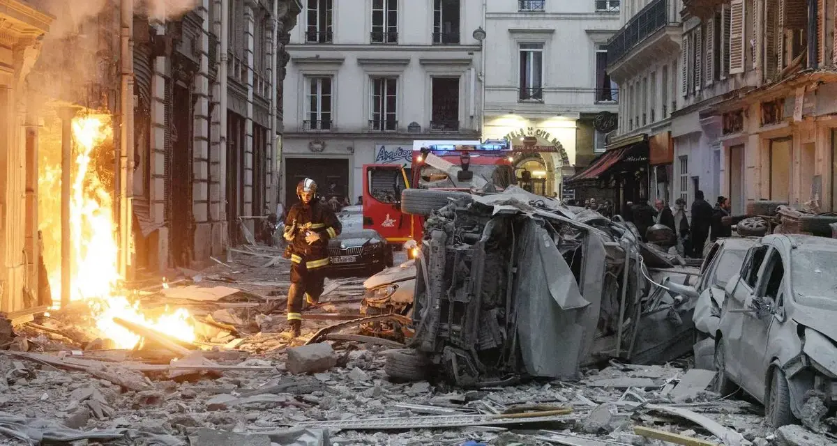 Un pompier avance dans les décombres d'une explosion gaz Paris. Des voitures détruites et des flammes ravagent la rue.