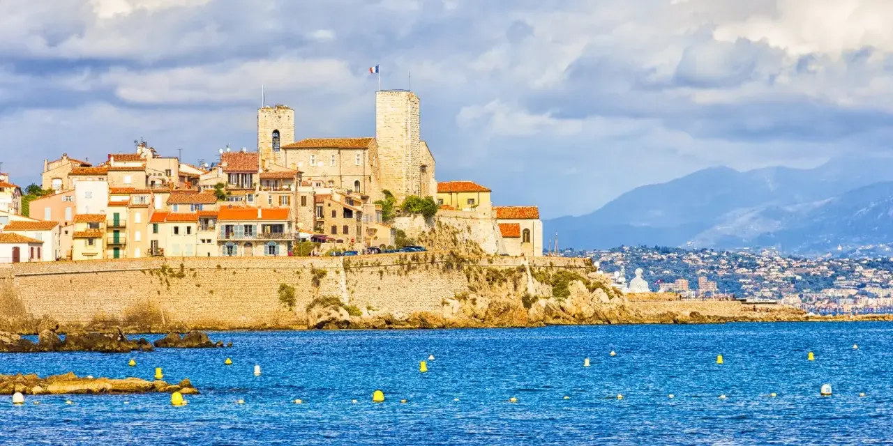 Vista de la ciudad amurallada de Antibes, Francia, con sus torres y edificios coloridos sobre un acantilado, bañada por el mar azul.