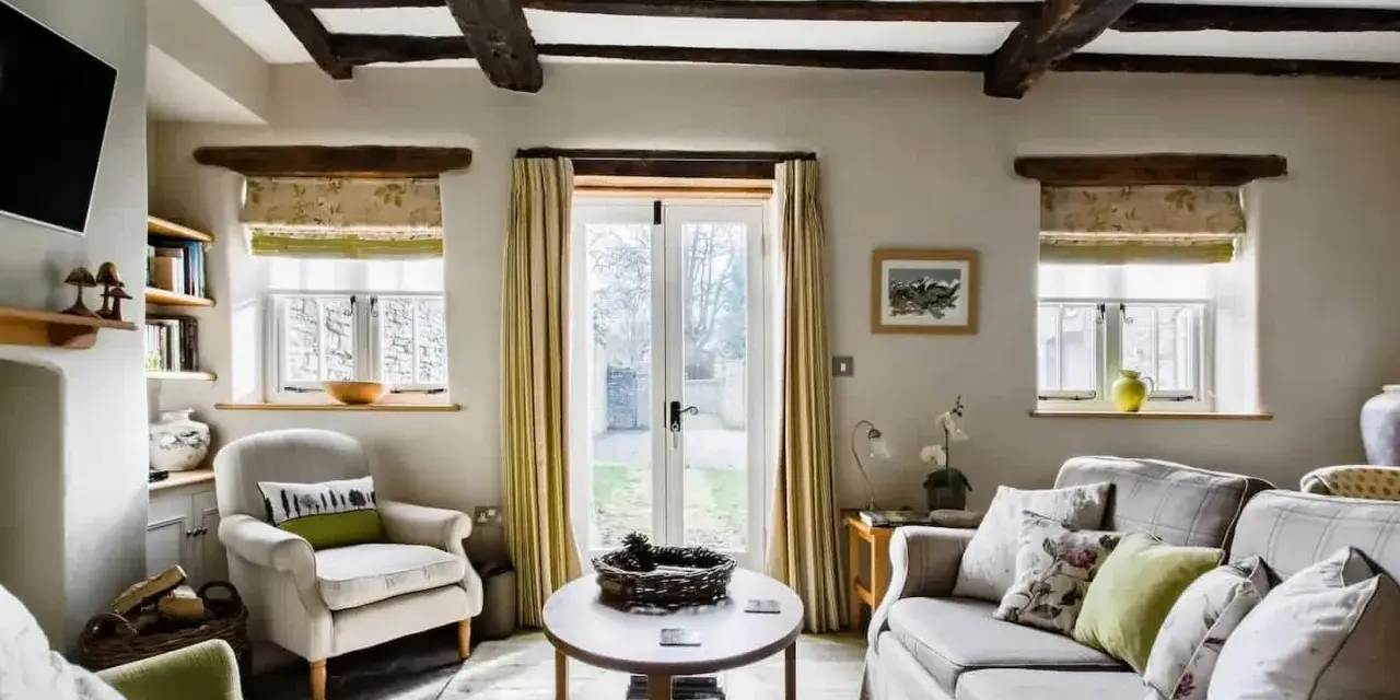 Salon confortable d'un maison cottage anglais, avec poutres apparentes, fauteuils douillets et vue sur le jardin.