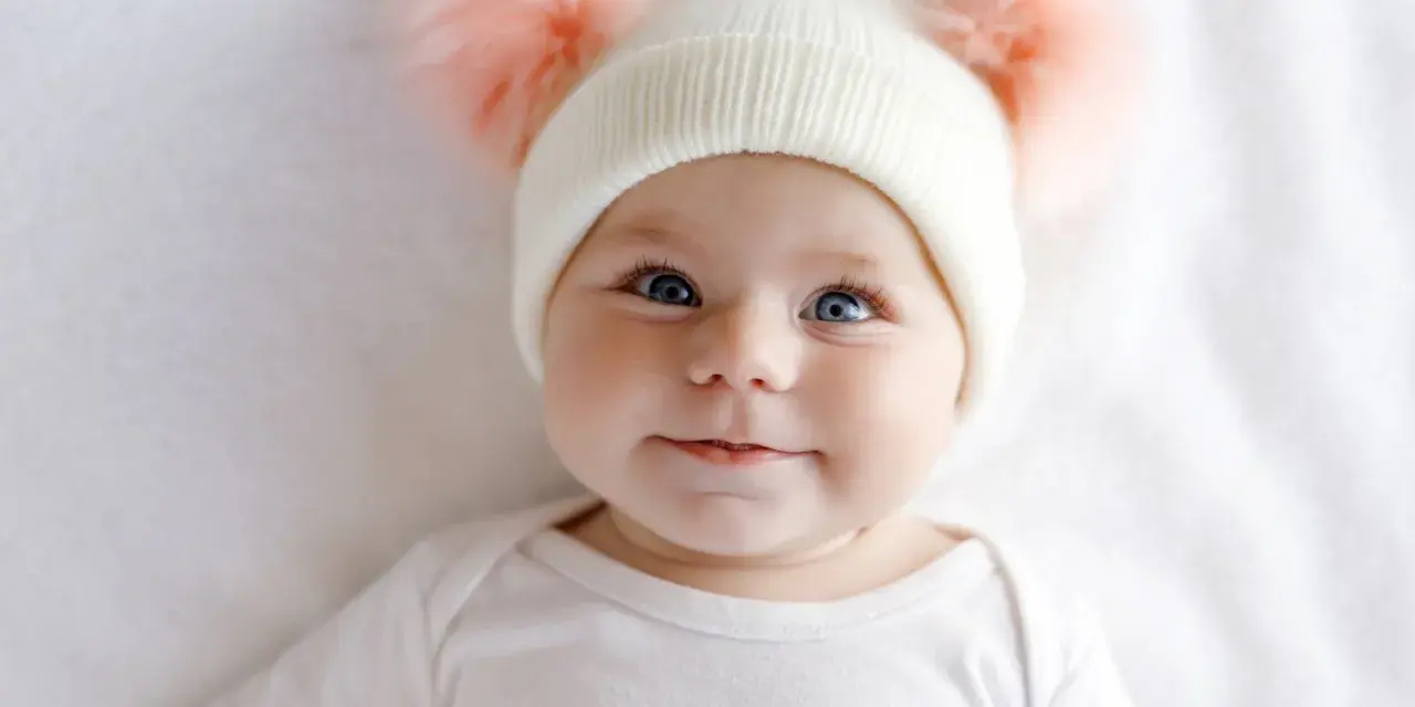 Ein süßes Baby mit blauen Augen und einer Mütze mit Bommeln. Man fragt sich, welche Augenfarbe bekommt mein Kind.