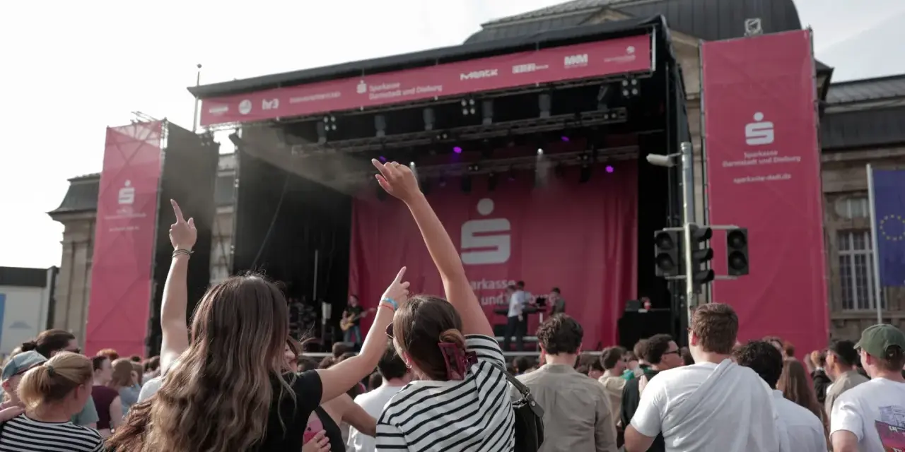 Menschen jubeln bei einem Open-Air-Konzert vor einer Bühne mit Sparkassen-Logo.
