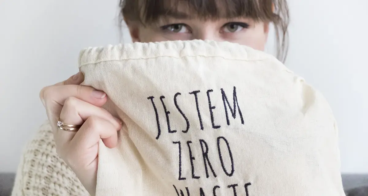 Sylwia Majcher, z uśmiechem ukrytym za torbą z napisem "Jestem Zero Waste", pokazuje swoje zaangażowanie w ekologię.