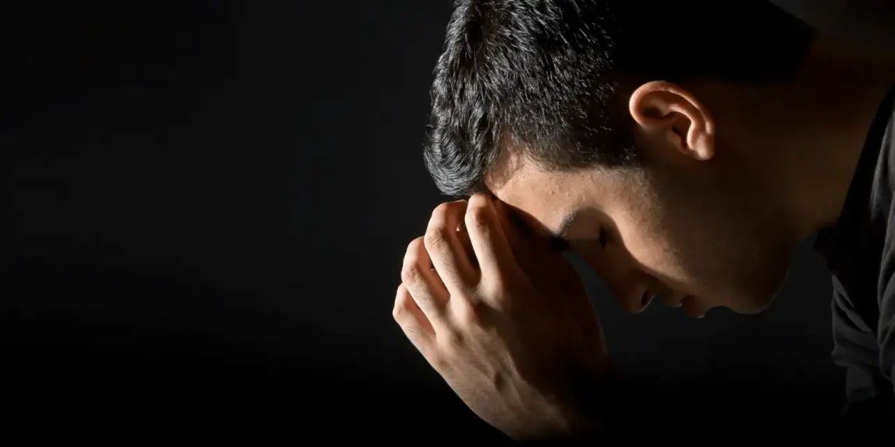 A man bows his head in prayer, hands clasped, reflecting the repentance meaning in the bible.