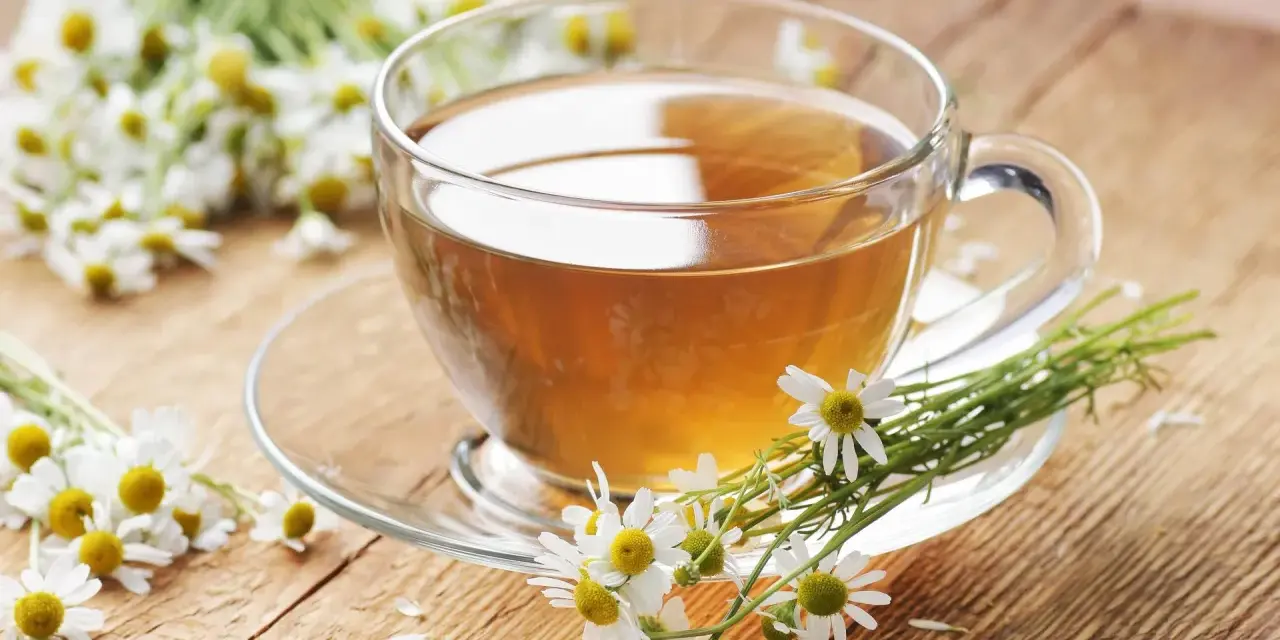 Une tasse de tisane de camomille, idéale pour le rhume traitement, entourée de fleurs fraîches sur un fond en bois.