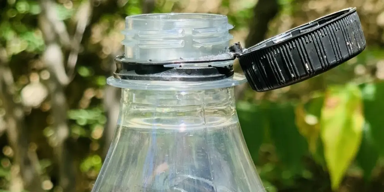 Nakrętki od butelek są przytwierdzone, by zapobiec ich zgubieniu i ułatwić ponowne zakręcenie. Widoczny fragment plastikowej butelki z otwartą, czarną nakrętką.
