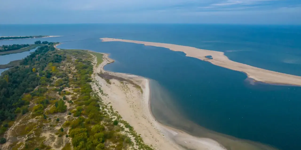 Piękne wybrzeże bałtyckie z piaszczystą mierzeją, zielonymi wydmami i spokojną wodą.